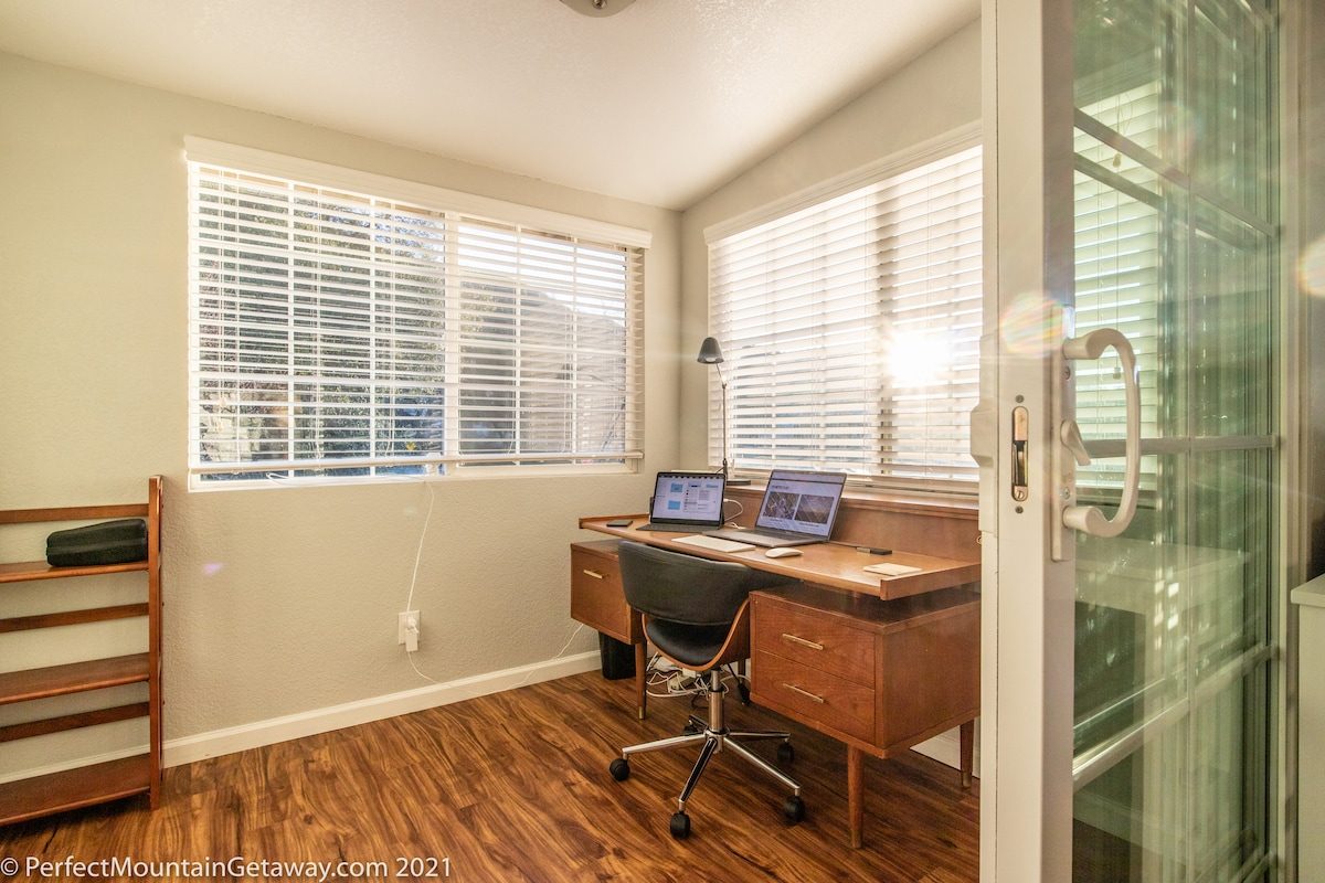 Office with desk, laptop, lamp, and windows with blinds.